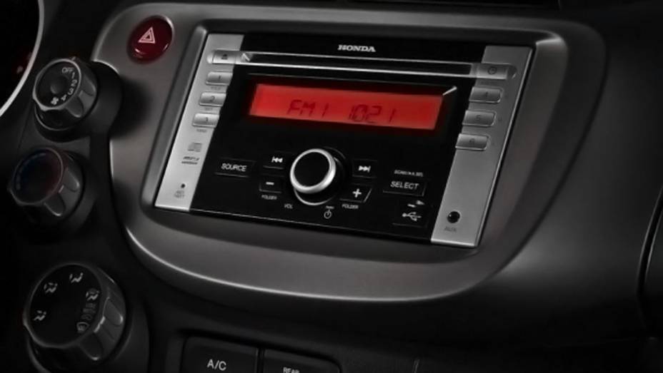 Rádio da versão LX está integrado ao console e vem com entrada USB | <a href="https://preprod.quatrorodas.abril.com.br/carros/lancamentos/honda-fit-2013-680204.shtml" rel="migration">Leia mais</a>