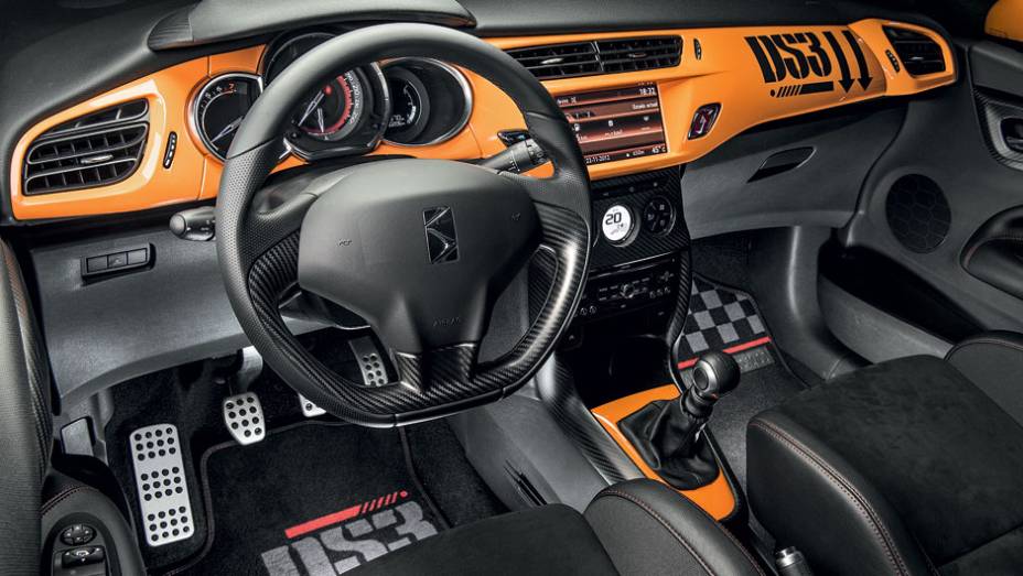 Tapetes, painel e volante seguem a decoração da carroceria, com fibra de carbono, pintura laranja e grafismo militar | <a href="https://preprod.quatrorodas.abril.com.br/carros/testes/citroen-ds3-racing-728659.shtml" rel="migration">Leia mais</a>