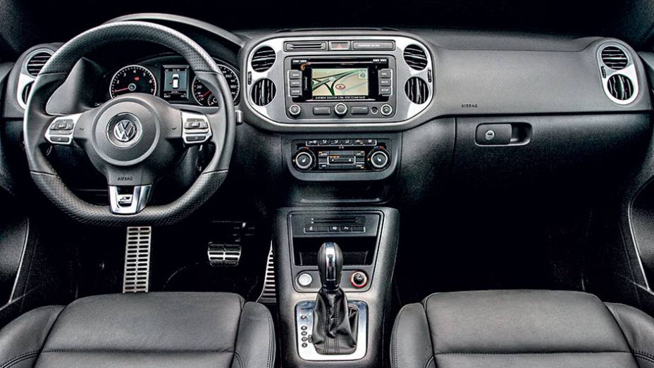 Interior possui volante de tr&ecirc;s raios com base achatada | <a href="https://preprod.quatrorodas.abril.com.br/carros/lancamentos/vw-tiguan-r-line-726908.shtml" rel="migration">Leia mais</a>