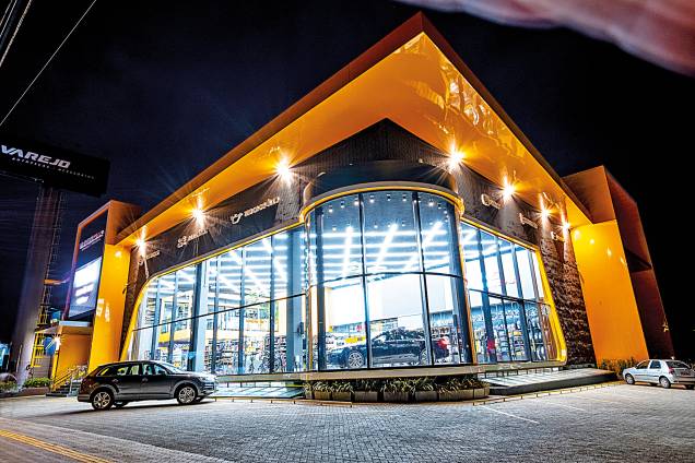 Temática de carro é seguida na oferta de roupas, tênis, acessórios e até de perfumes. Fachada se destaca das demais pela área envidraçada, pelo carro em exposição dentro da loja e o telão de led Temática de carro é seguida na oferta de roupas, tênis, acessórios e até de perfumes. Fachada se destaca das demais pela área envidraçada, pelo carro em exposição dentro da loja e o telão de led