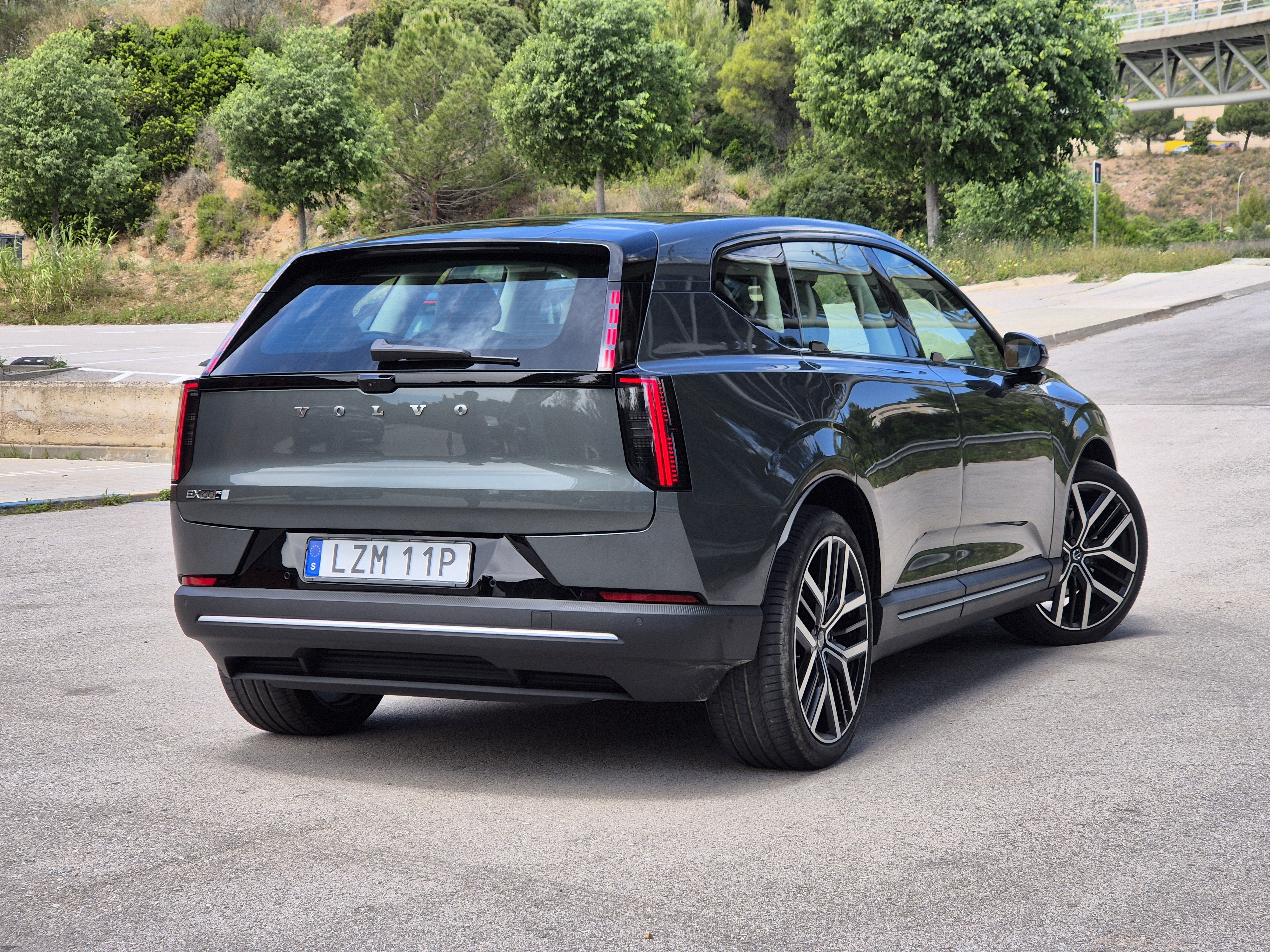 SUV Volvo EX60 cinza-escuro estacionado em uma rua asfaltada, visto por tr&aacute;s e lateralmente. As lanternas traseiras verticais e a placa 
