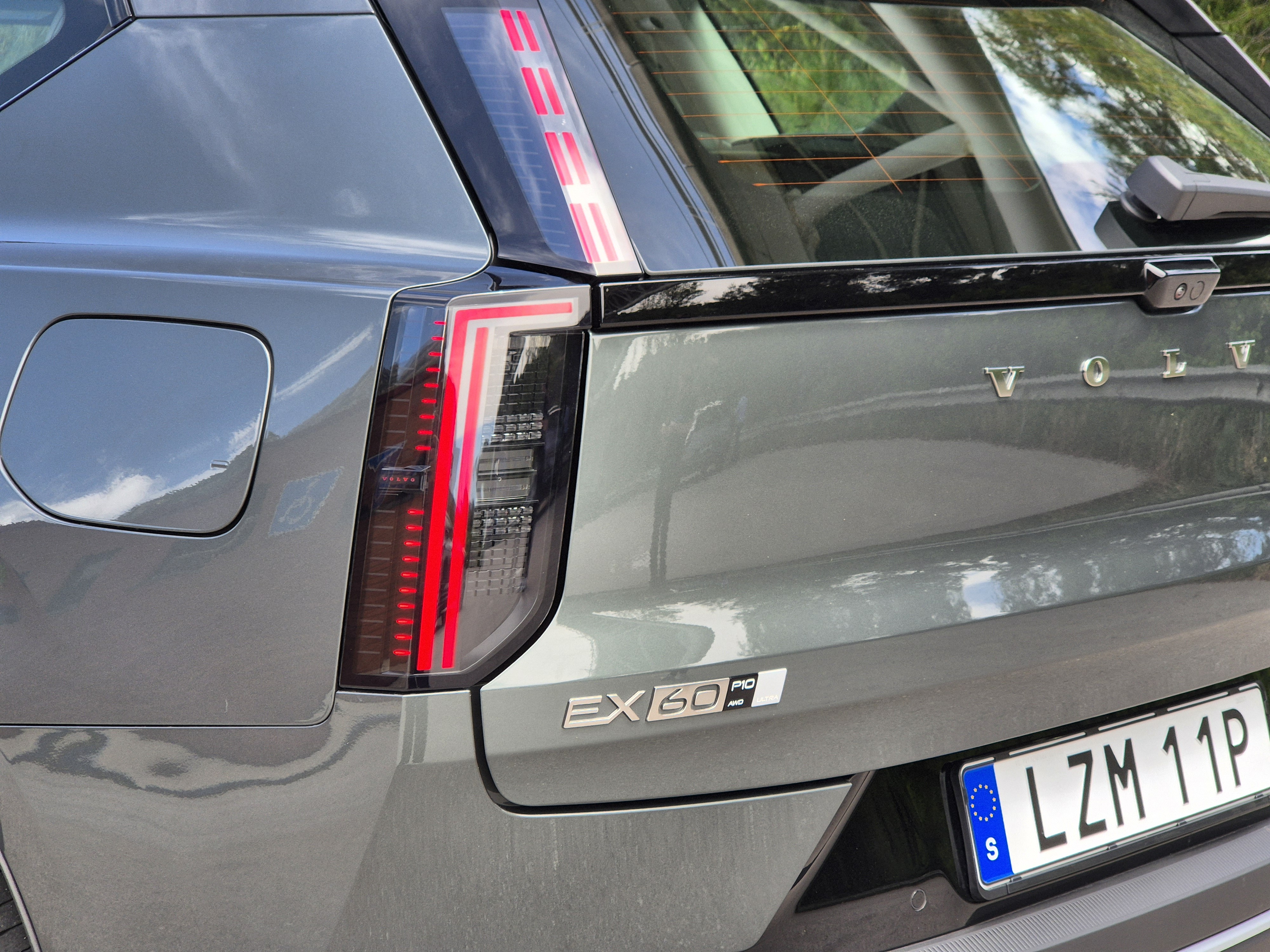 Traseira de um Volvo EX60 cinza-esverdeado, com lanternas verticais de LED acesas em vermelho, tampa do porta-malas com o nome 