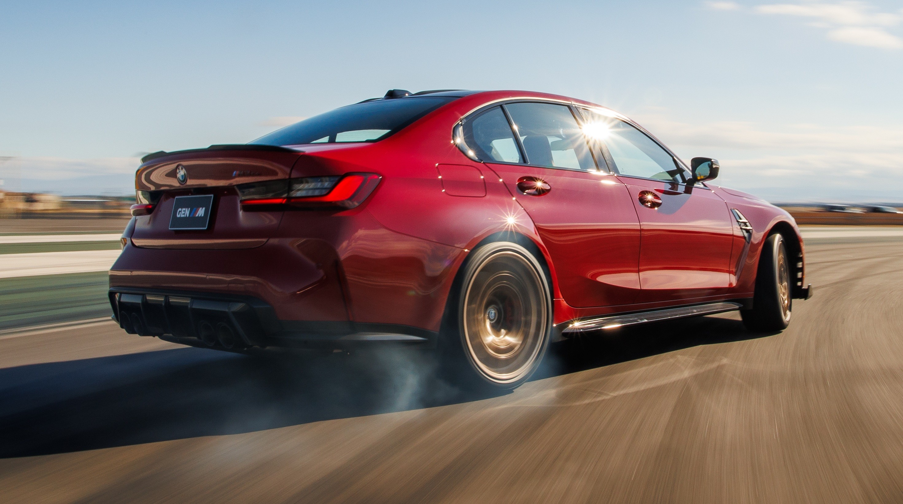 Carro esportivo vermelho em movimento r&aacute;pido, visto de tr&aacute;s e lateral, com fuma&ccedil;a saindo do pneu traseiro esquerdo. O sol reflete na janela, e o fundo desfocado indica alta velocidade em uma pista