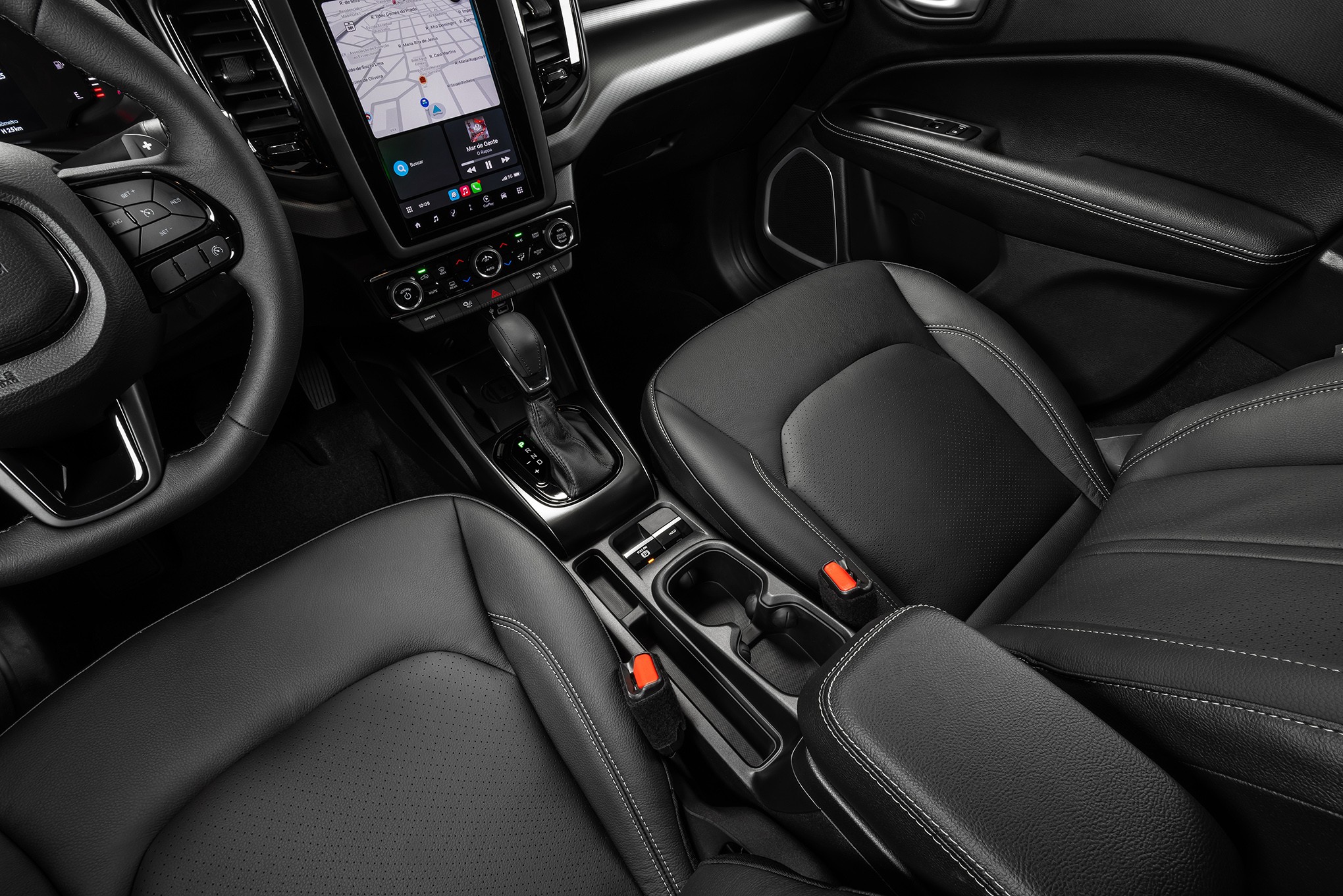 Interior de carro moderno com bancos de couro preto, console central com porta-copos, c&acirc;mbio autom&aacute;tico e tela multim&iacute;dia exibindo mapa de navega&ccedil;&atilde;o. Volante multifuncional &agrave; esquerda