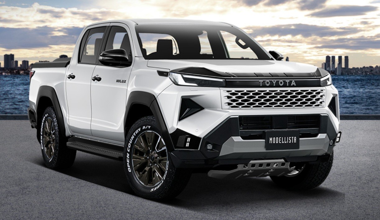 Picape Toyota Hilux branca com kit Modellista, grade frontal preta e cromada, para-choque robusto, rodas escuras e pneus off-road, estacionada em asfalto com fundo de mar e cidade
