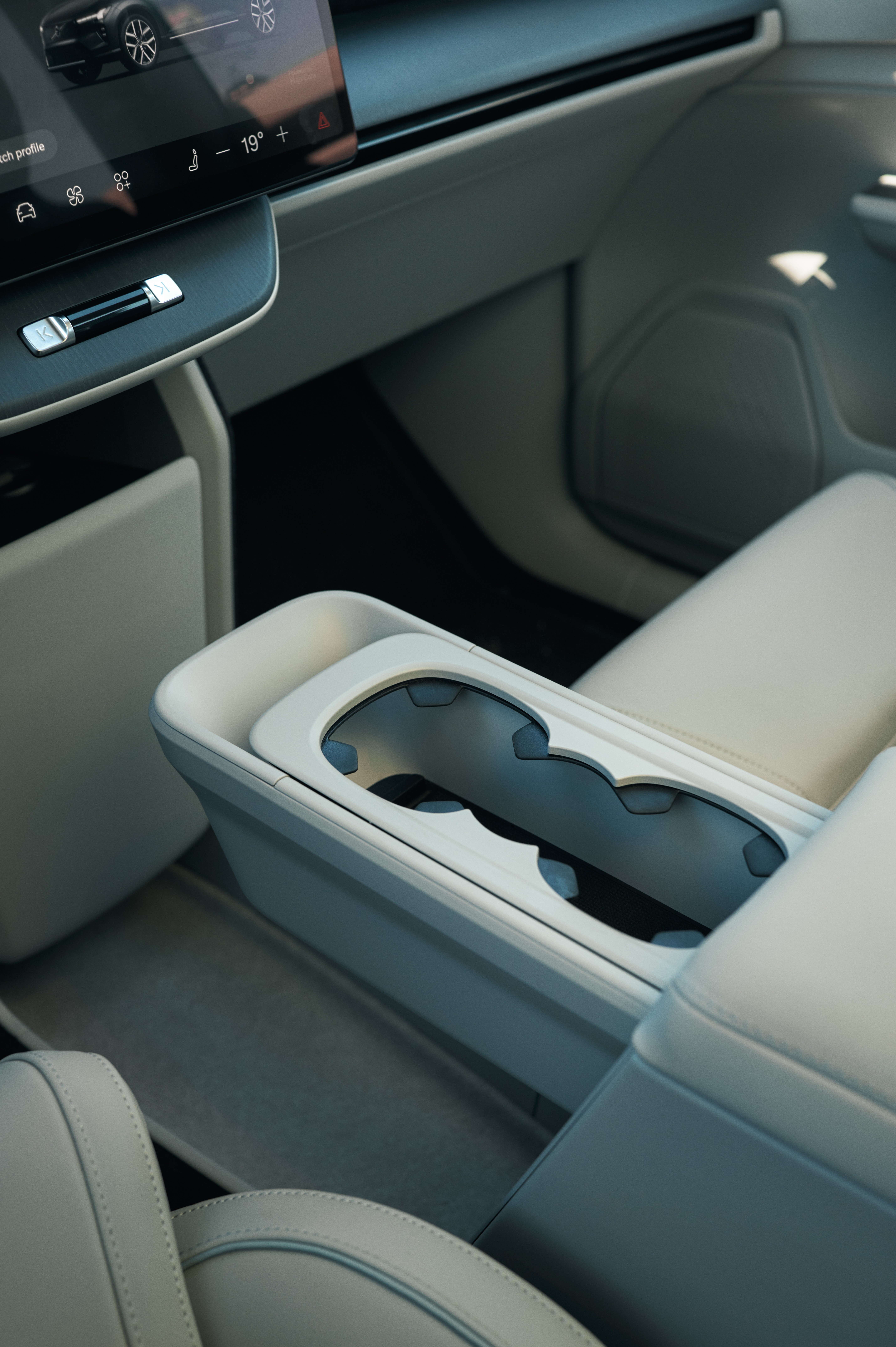 Interior de carro moderno com console central bege claro, porta-copos duplo e tela multim&iacute;dia exibindo um carro e temperatura de 19 graus