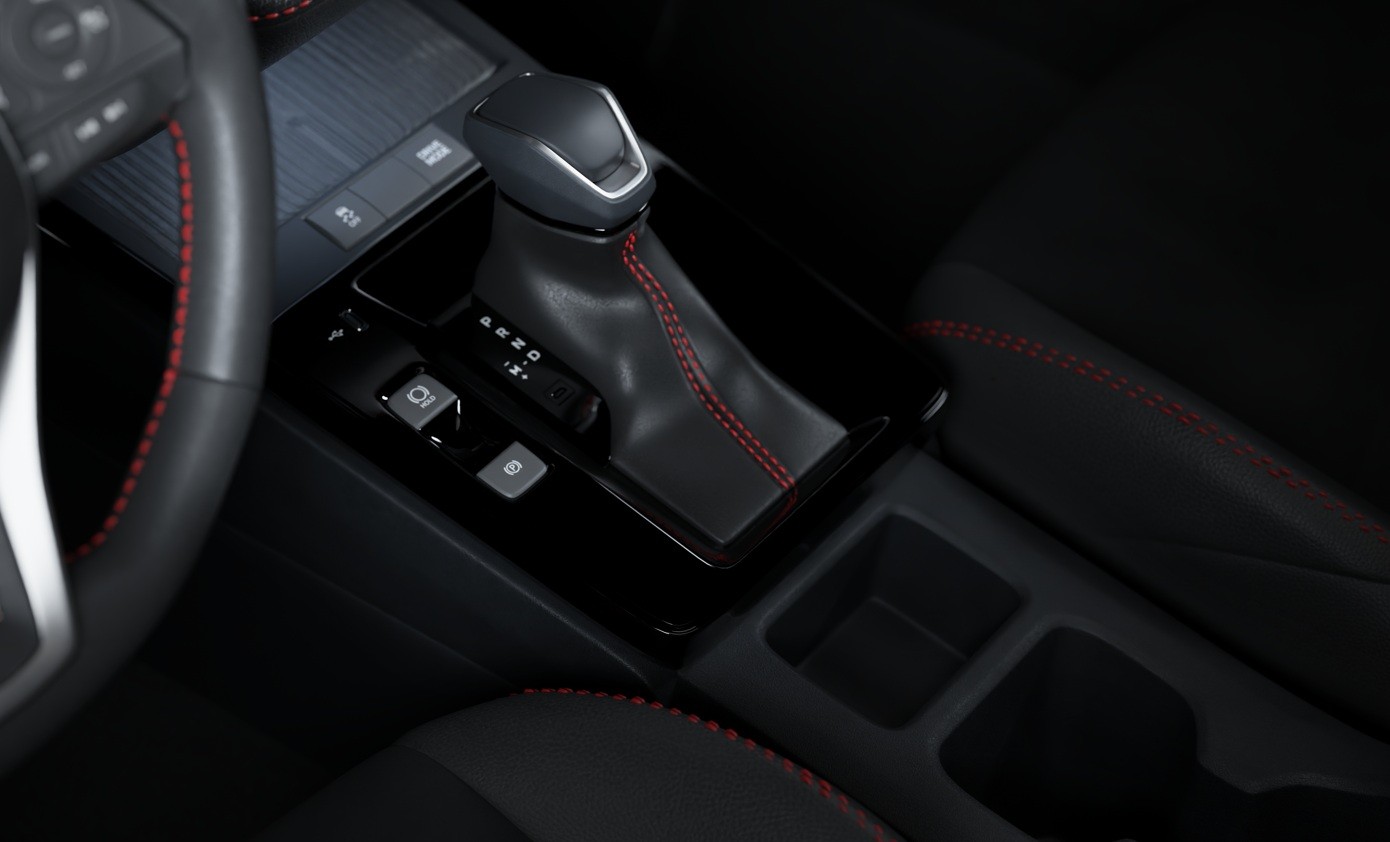 Interior de um carro com c&acirc;mbio autom&aacute;tico preto e costura vermelha, volante parcialmente vis&iacute;vel &agrave; esquerda com costura vermelha, e assento escuro com costura vermelha &agrave; direita. Detalhes do console central incluem bot&otilde;es e porta-copos.