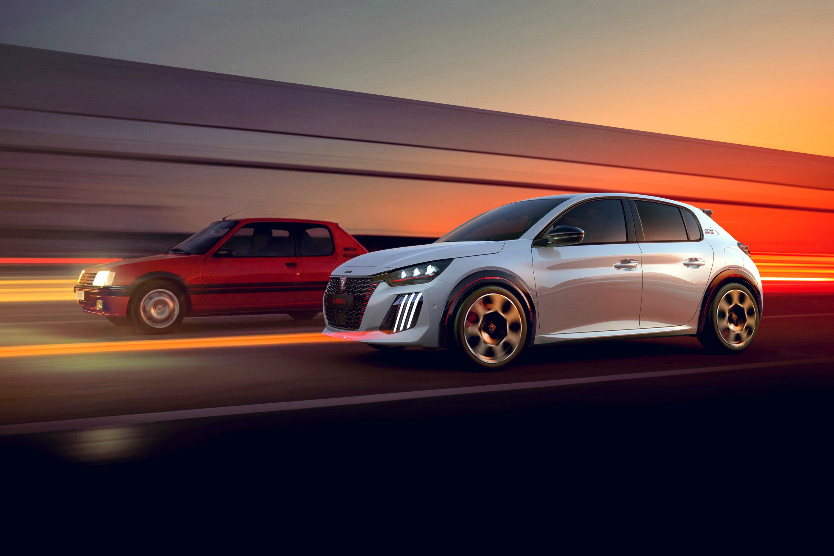 Dois carros Peugeot em movimento, um modelo antigo vermelho &agrave; esquerda e um moderno branco &agrave; direita, com luzes de LED acesas, em uma estrada com o c&eacute;u alaranjado do p&ocirc;r do sol ao fundo