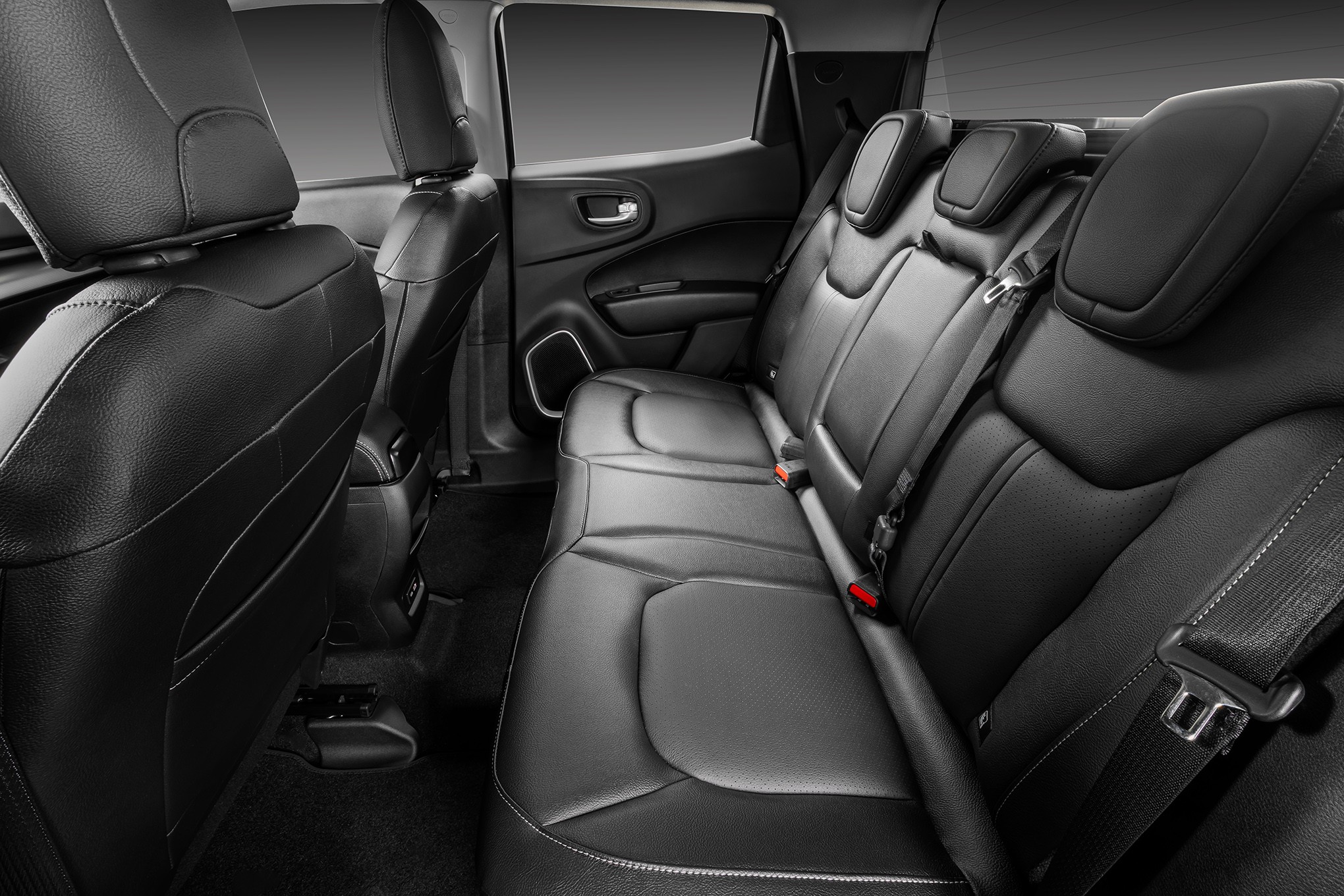 Interior de carro com bancos traseiros de couro preto, cintos de seguran&ccedil;a vis&iacute;veis e encostos de cabe&ccedil;a ajust&aacute;veis, destacando o conforto e espa&ccedil;o