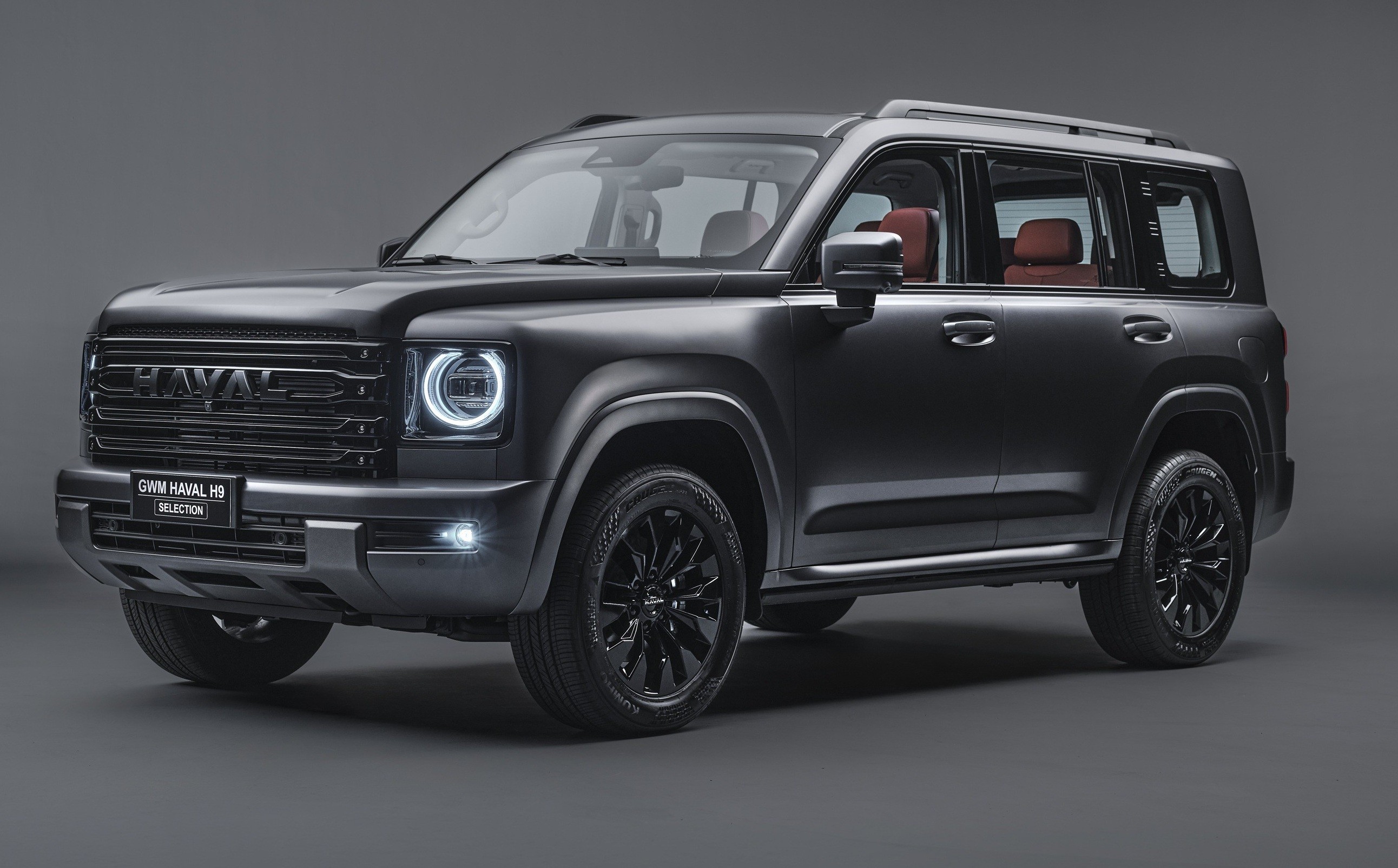 SUV Haval H9 preto fosco, com far&oacute;is redondos acesos, grade frontal escura e rodas pretas, exibindo interior com bancos marrons