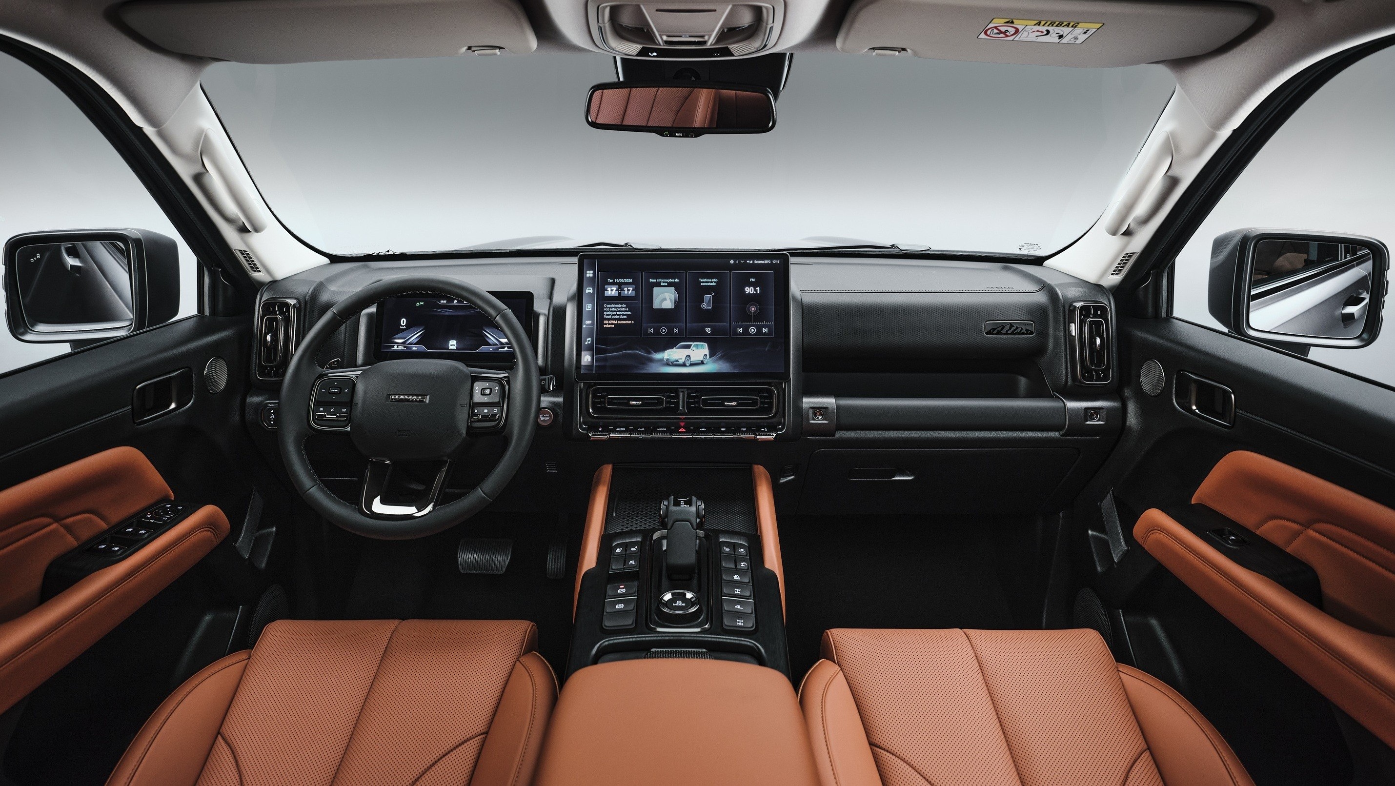 Interior de um carro moderno com bancos de couro marrom-claro e painel preto. O volante multifuncional est&aacute; &agrave; esquerda, e uma grande tela multim&iacute;dia central exibe um carro branco. O console central possui bot&otilde;es e alavanca de c&acirc;mbio.