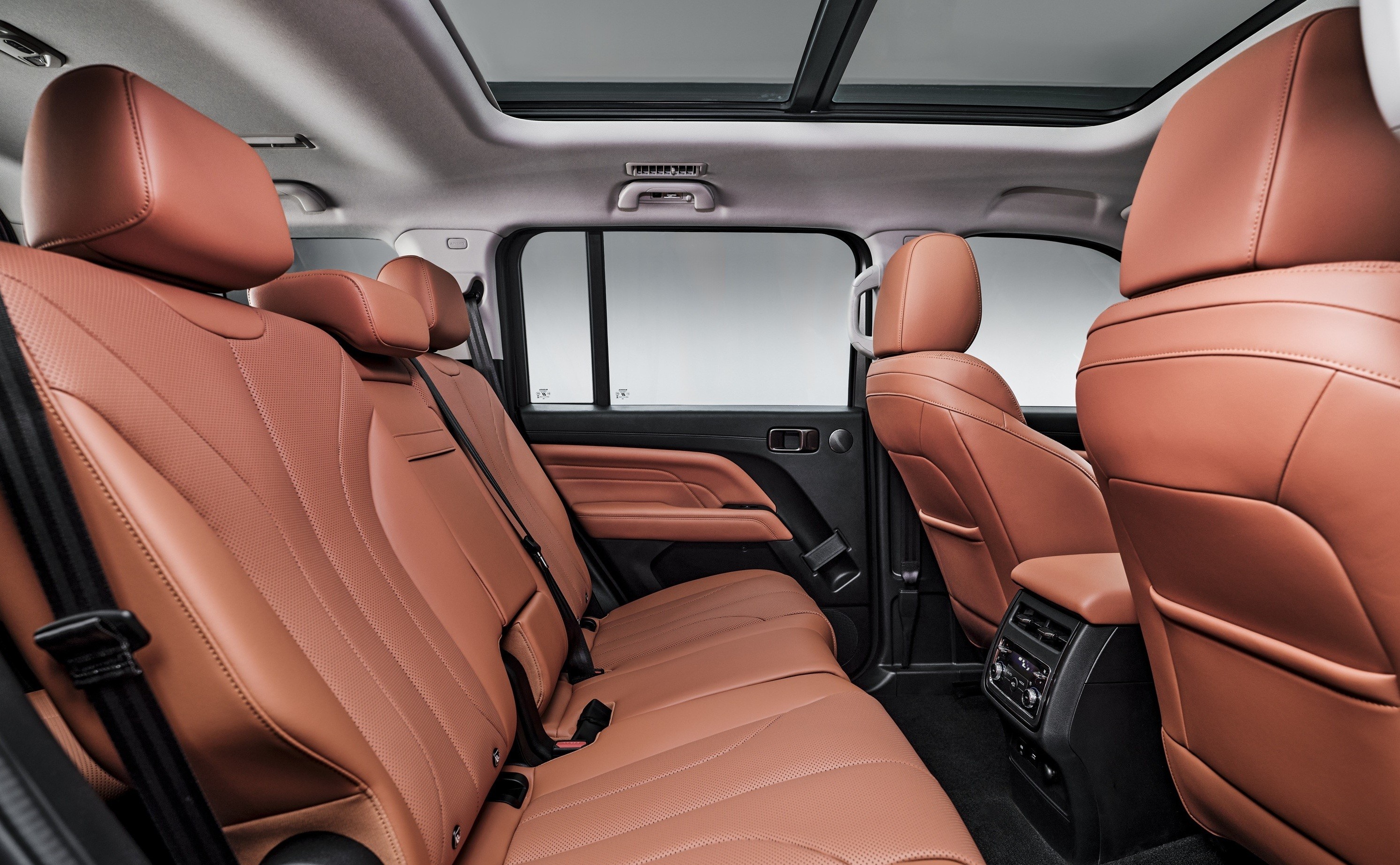 Interior de um carro com bancos de couro marrom-claro, incluindo a segunda e terceira fileiras. O teto solar panor&acirc;mico est&aacute; vis&iacute;vel, e h&aacute; um painel de controle de ar-condicionado na parte traseira do console central