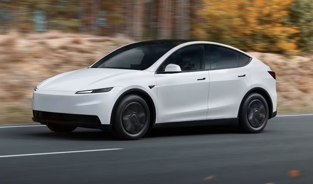 Carro el&eacute;trico branco, modelo Tesla, em movimento r&aacute;pido sobre uma estrada asfaltada com faixa branca. O ve&iacute;culo tem teto preto e rodas escuras. O fundo est&aacute; desfocado, com tons de marrom e verde, sugerindo vegeta&ccedil;&atilde;o