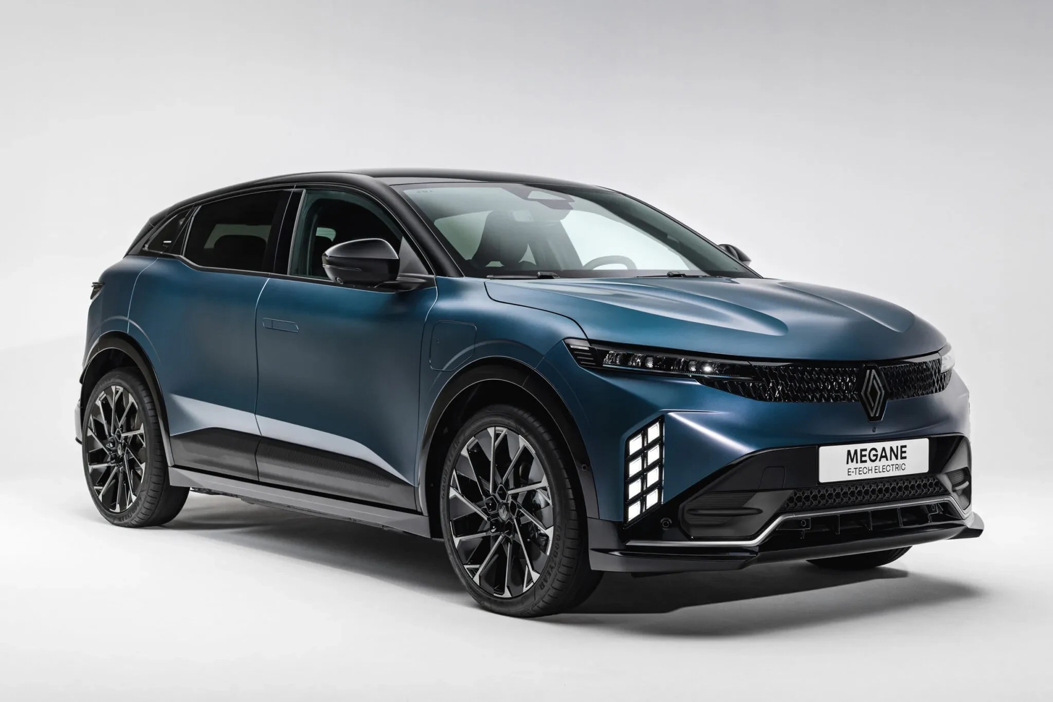Carro Renault Megane E-Tech Electric azul-petróleo com teto preto, faróis e luzes diurnas em LED, rodas esportivas pretas, estacionado em estúdio branco
