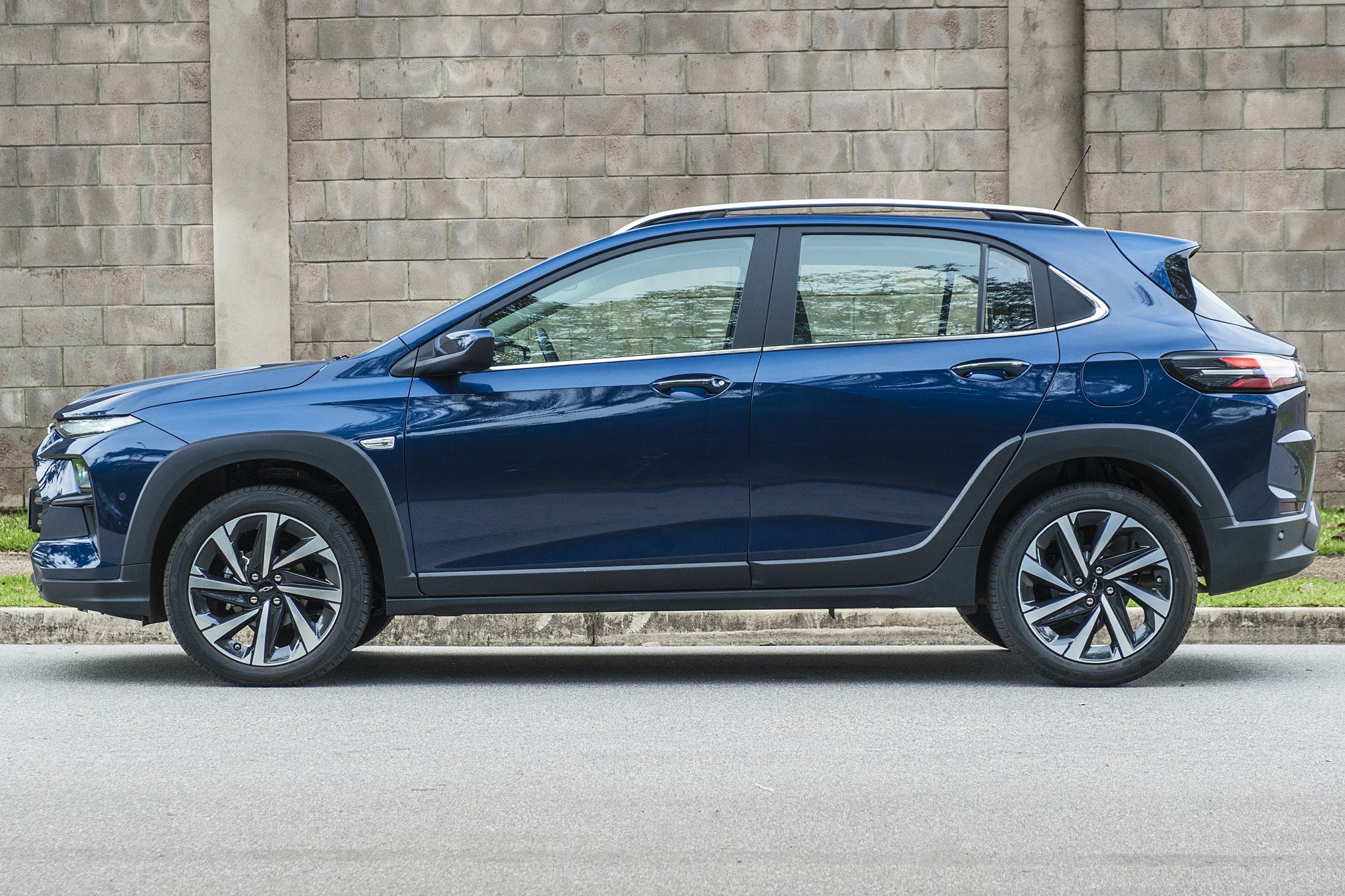 Carro SUV azul escuro, modelo Fiat Pulse, estacionado de perfil em uma rua asfaltada, com uma parede de tijolos cinzas ao fundo