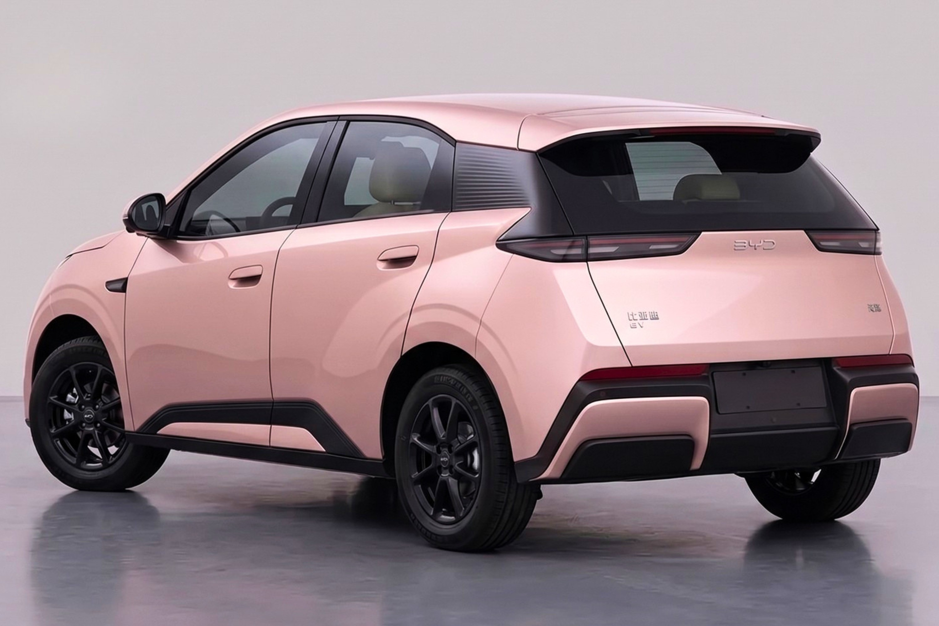 Carro compacto el&eacute;trico rosa-claro com detalhes em preto, visto de traseira e lateral, sobre piso cinza. Possui rodas pretas, lanternas traseiras horizontais e para-choque com apliques pretos e rosa.