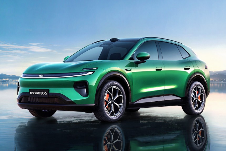 SUV elétrico verde-esmeralda com teto preto, refletido na superfície da água, contra um céu azul claro e montanhas distantes