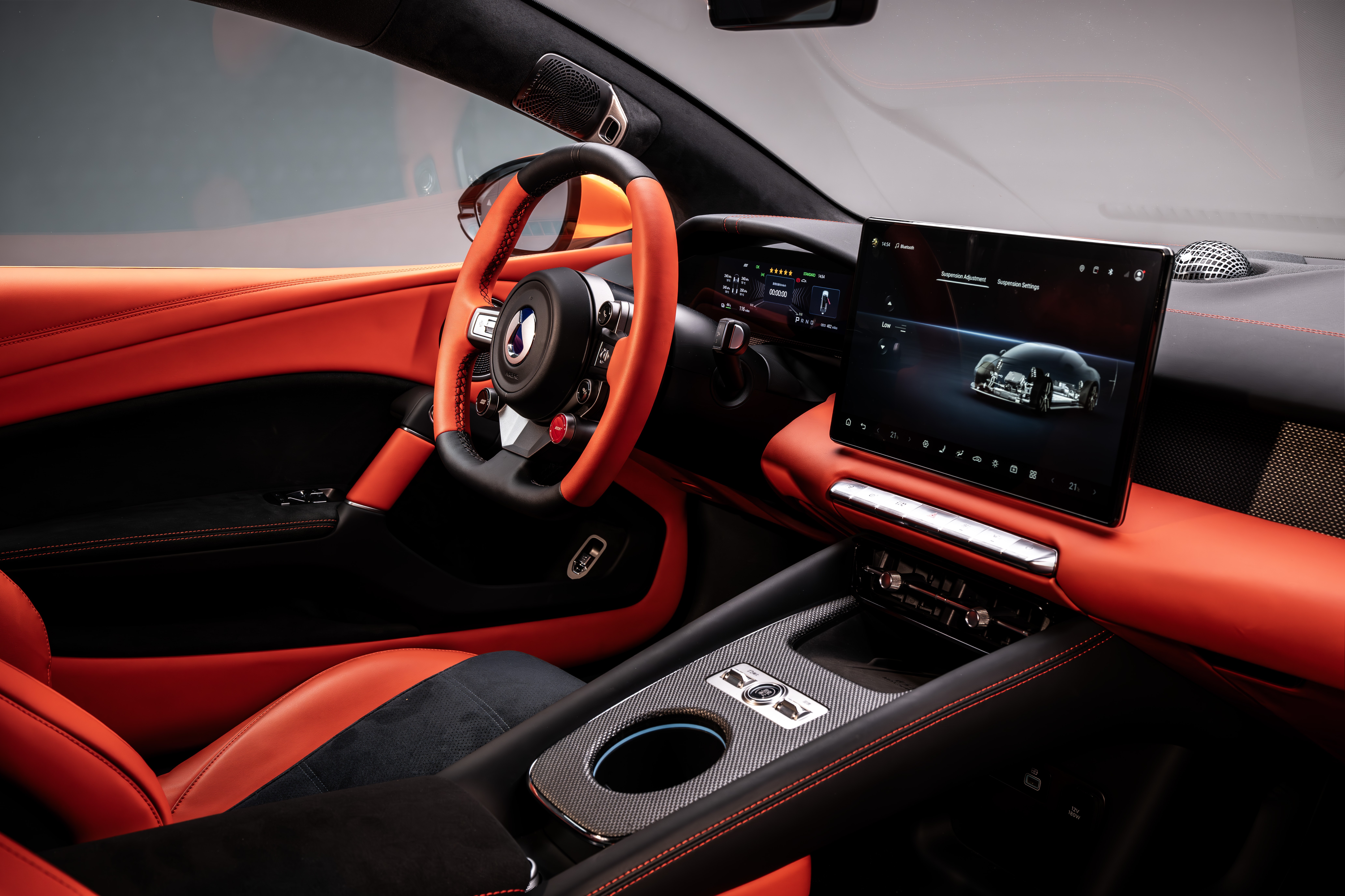 Interior de carro esportivo com estofamento laranja e preto, volante laranja e tela multim&iacute;dia exibindo um carro prateado