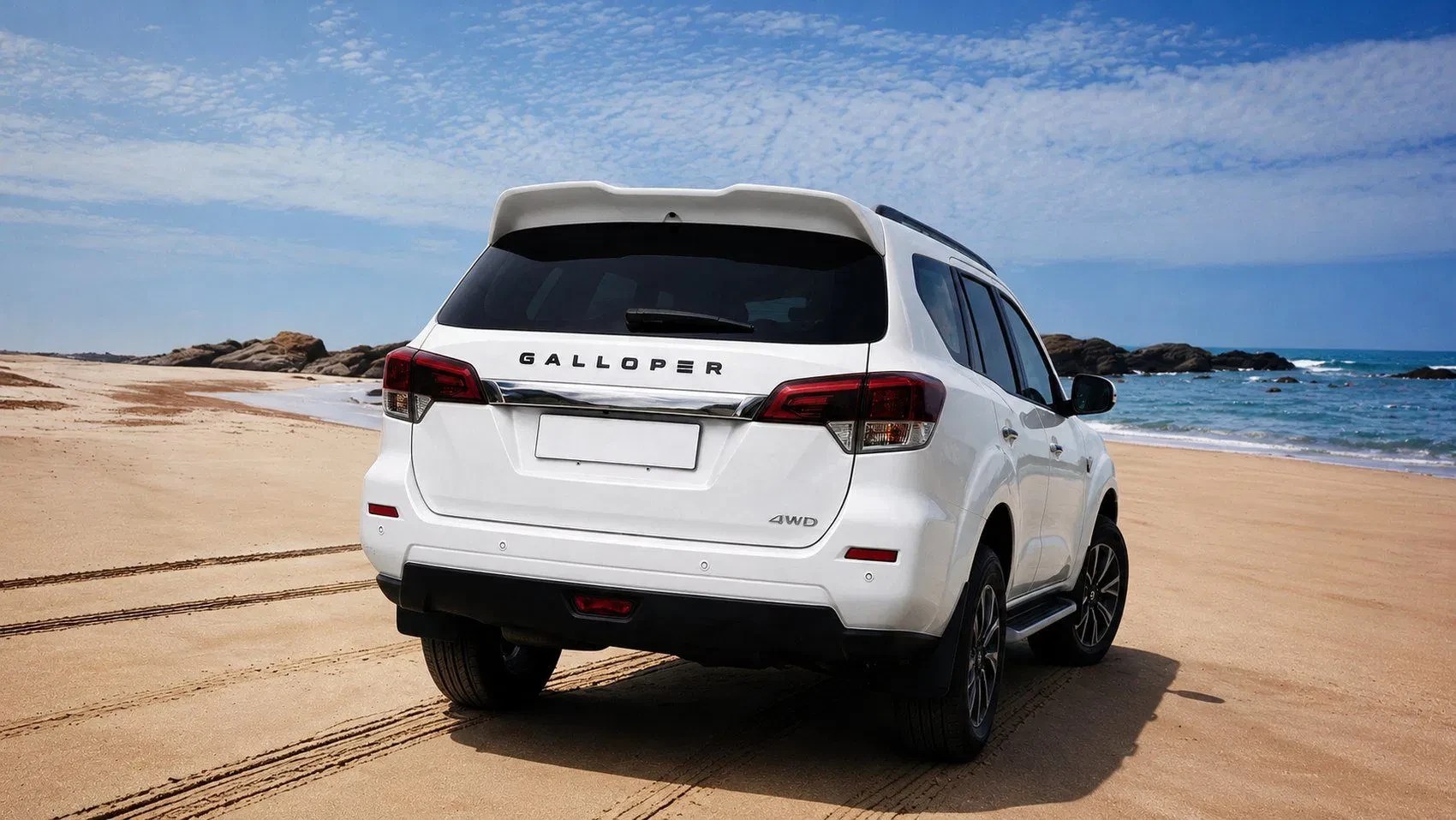 SUV branco Galloper estacionado na areia da praia, com o mar azul e rochas ao fundo sob um céu claro