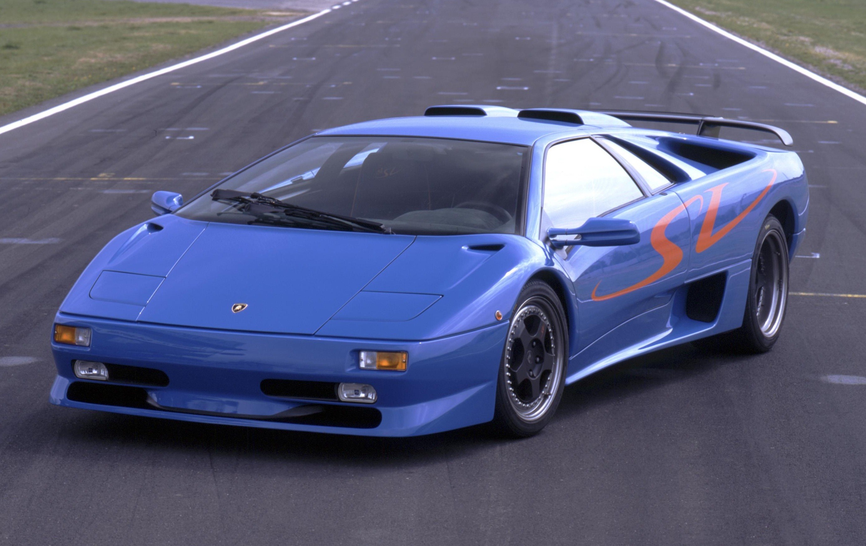 Carro esportivo Lamborghini Diablo azul com detalhes laranja SV na lateral, parado em uma pista de asfalto com faixas brancas