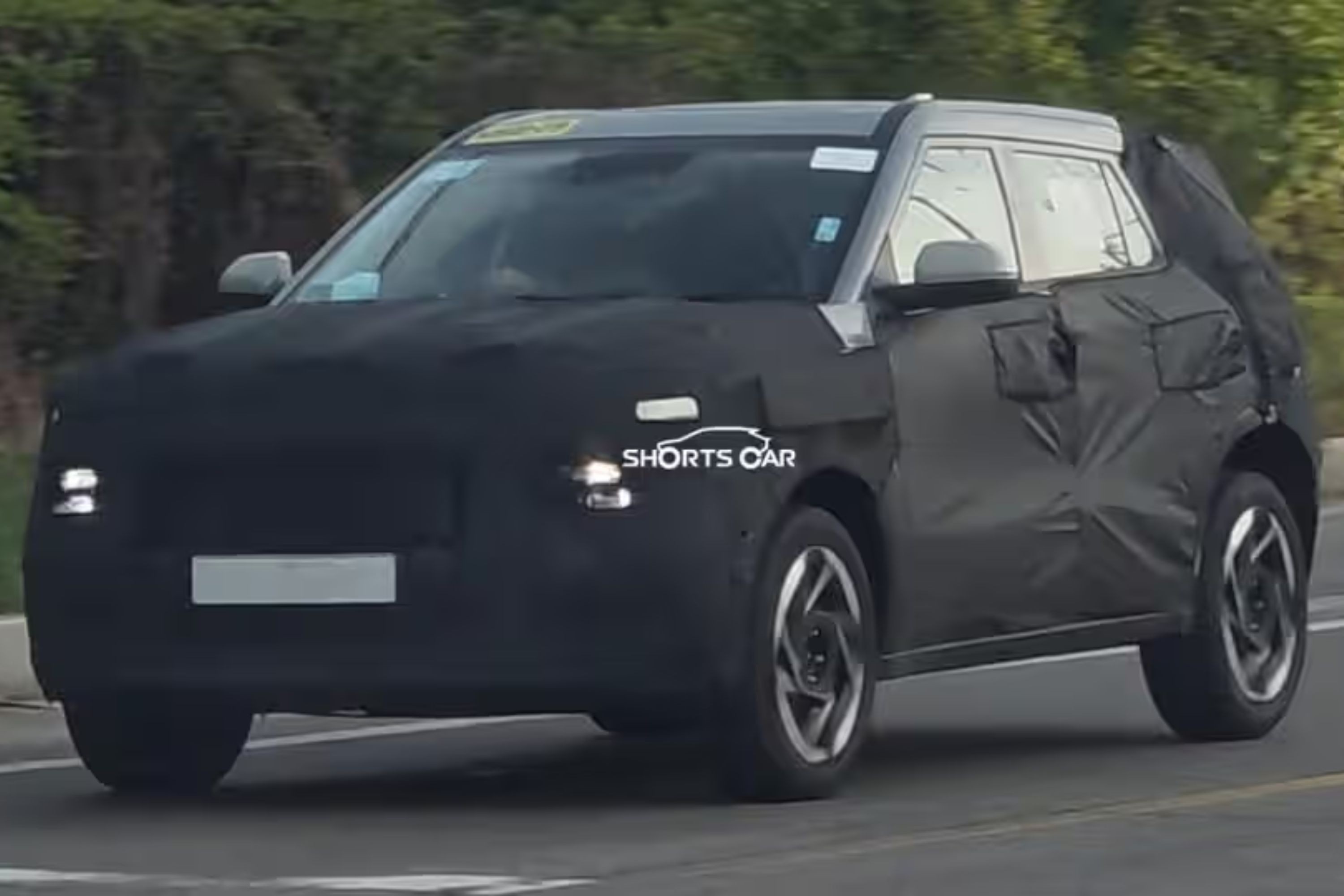 SUV camuflado preto com teto cinza claro e rodas de liga leve em movimento na rua, com far&oacute;is acesos e luzes diurnas em formato de H