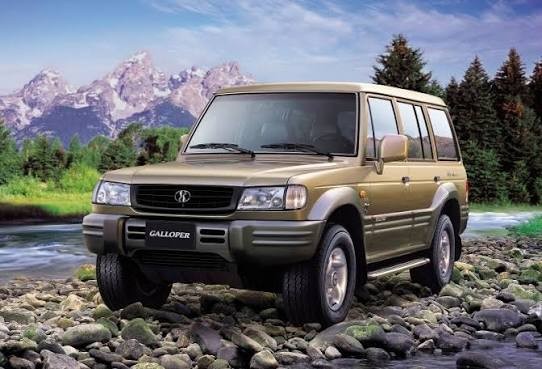 SUV Galloper dourado, com para-choques e molduras das rodas cinza-escuro, parado sobre pedras de rio. Ao fundo, montanhas nevadas, &aacute;rvores e c&eacute;u azul