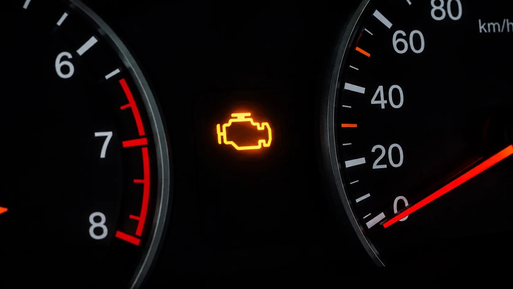 Painel de carro com luz de advertência do motor acesa em laranja, entre o conta-giros e o velocímetro, ambos com fundo preto e números brancos