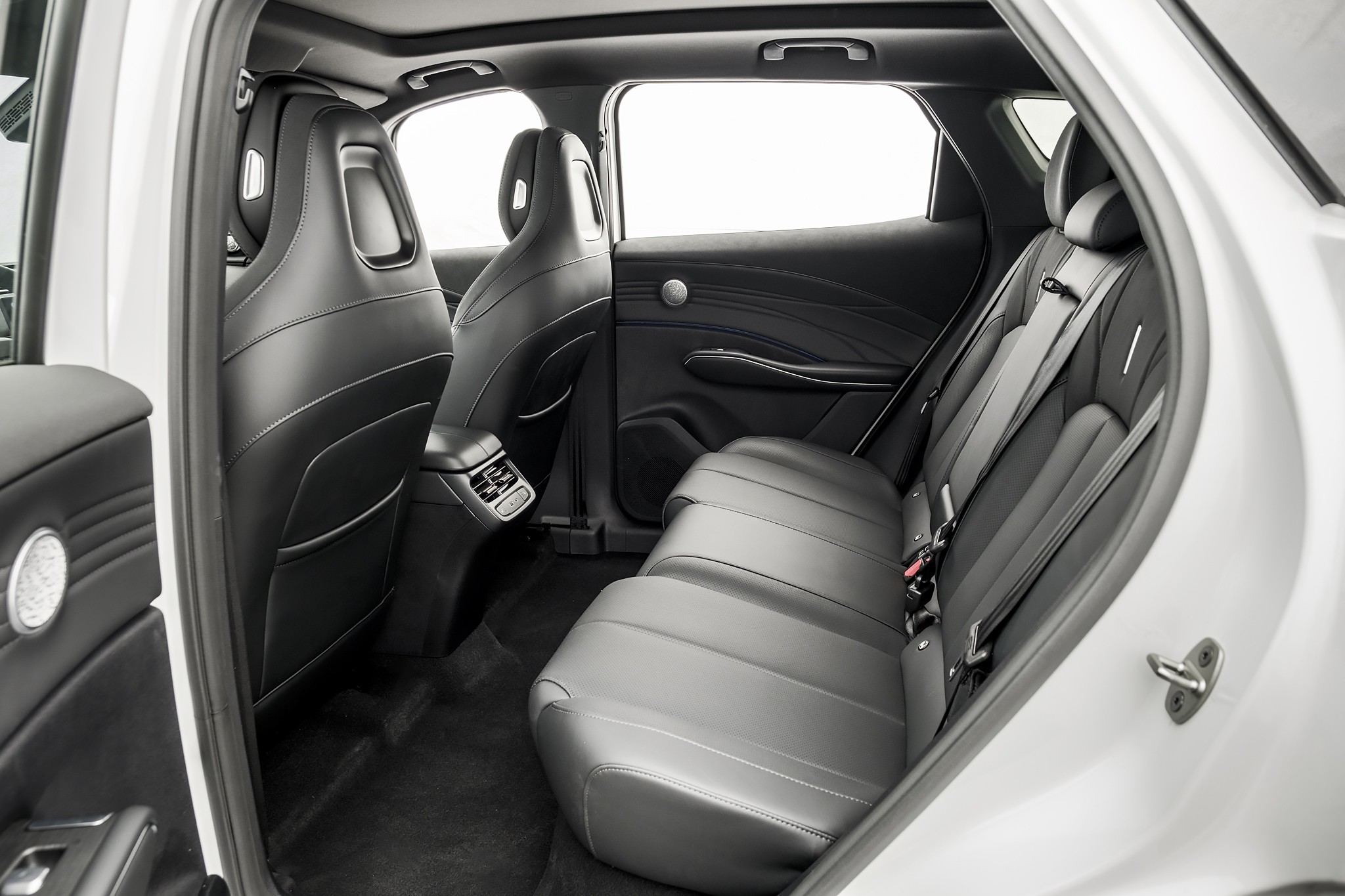 Interior de um carro, mostrando os bancos traseiros e a parte de tr&aacute;s dos bancos dianteiros, todos em couro preto com costuras brancas. O banco traseiro &eacute; inteiri&ccedil;o, com cintos de seguran&ccedil;a vis&iacute;veis. As portas t&ecirc;m acabamento preto e detalhes prateados. O teto solar e as janelas est&atilde;o vis&iacute;veis, com luz branca entrando. O piso &eacute; forrado com carpete escuro