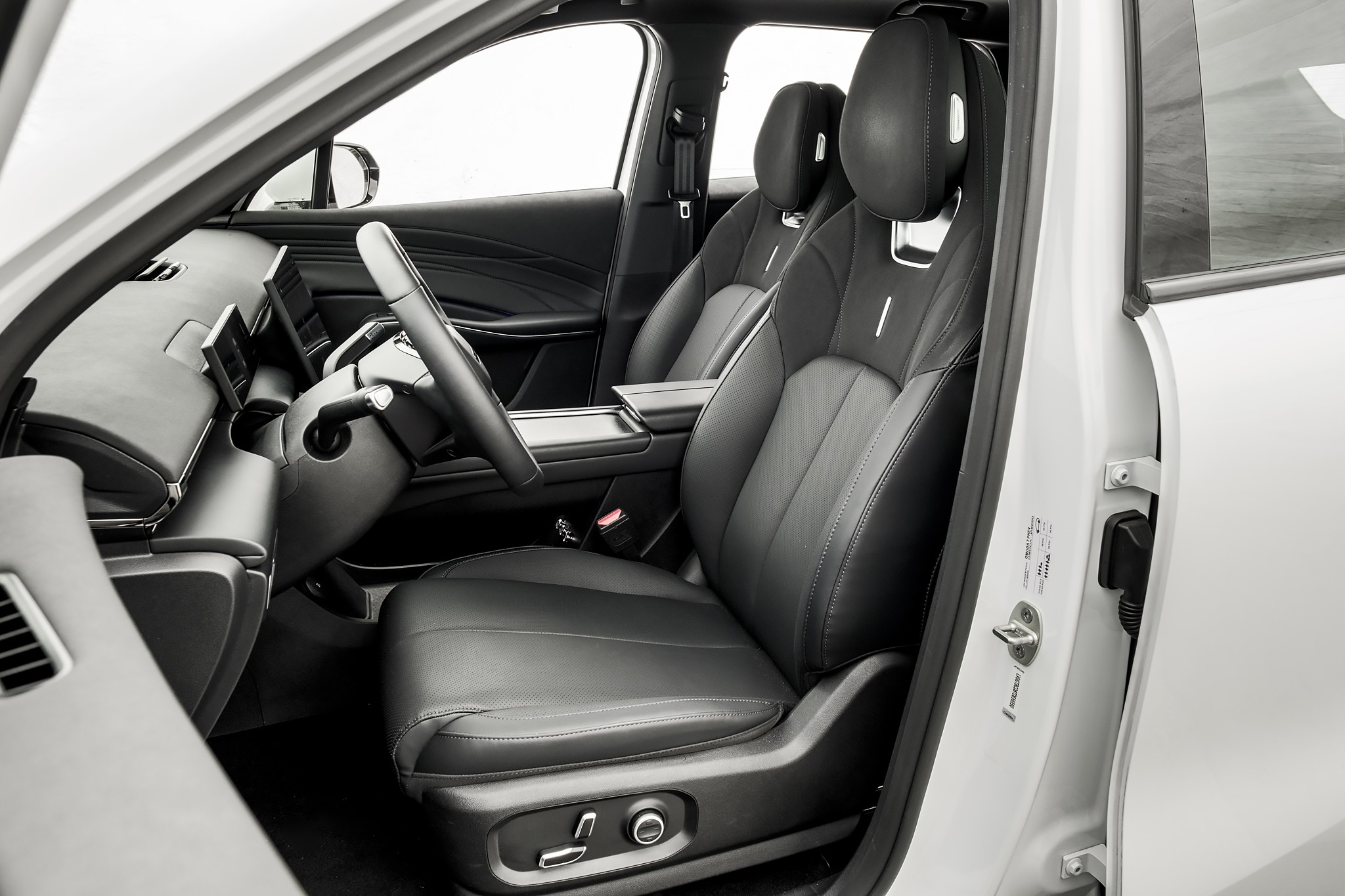 Interior de um carro moderno, com bancos de couro preto e detalhes em cinza. O volante e o painel digital s&atilde;o vis&iacute;veis, com a porta do motorista aberta, revelando a estrutura interna do ve&iacute;culo. O ambiente &eacute; claro e minimalista