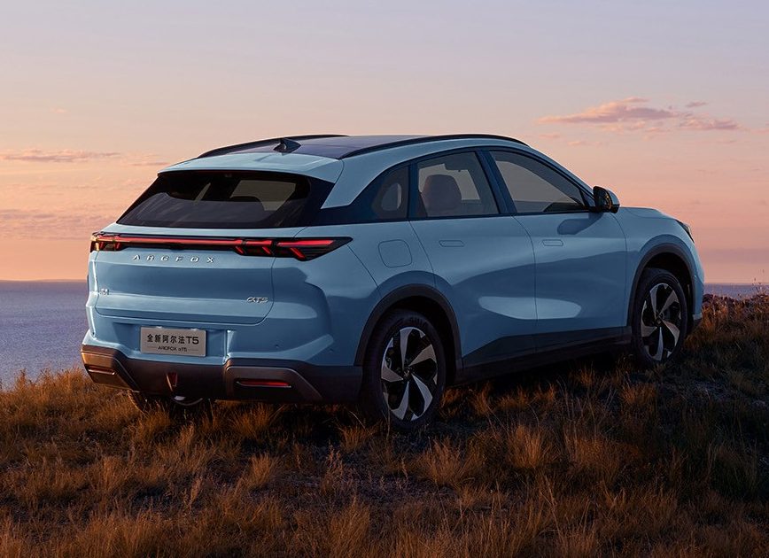 SUV azul claro estacionado em uma colina gramada com vista para o oceano ao p&ocirc;r do sol, c&eacute;u em tons de laranja e rosa