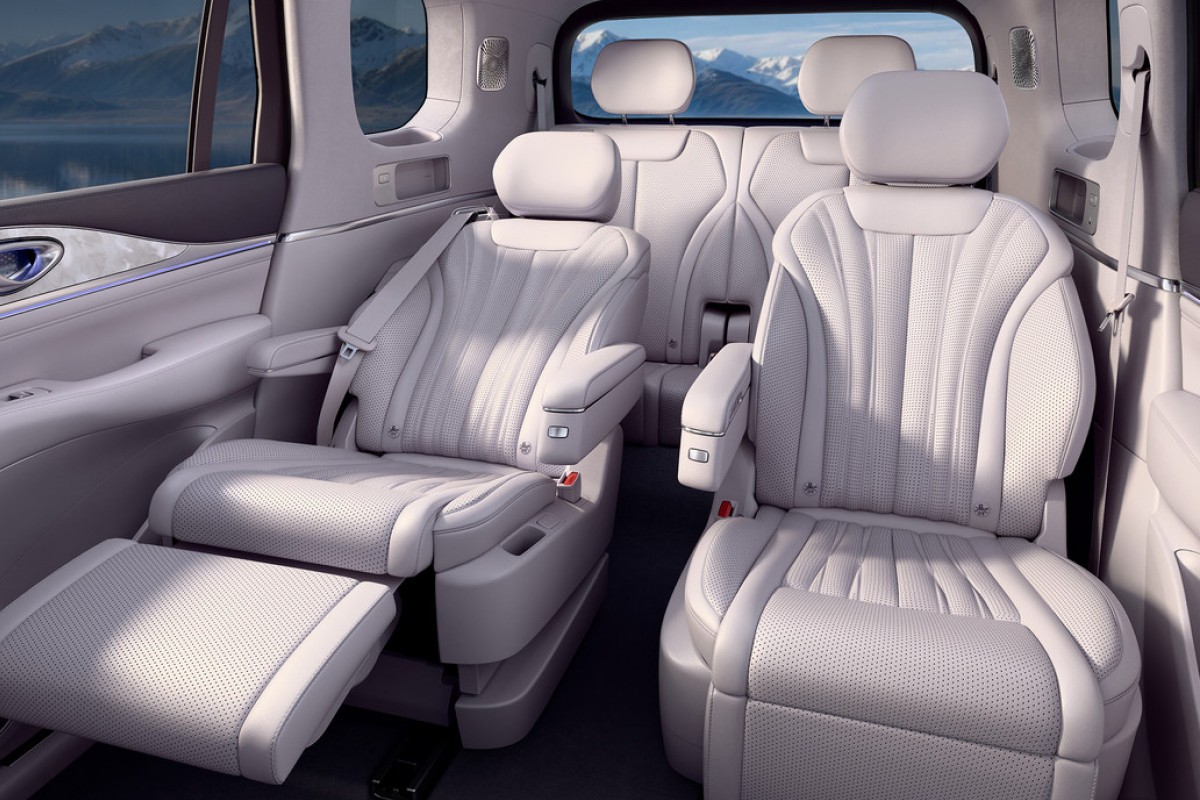 Interior de um carro de luxo com bancos de couro branco perfurado, o da esquerda reclinado com apoio para os p&eacute;s estendido, e o da direita em posi&ccedil;&atilde;o vertical. Ao fundo, montanhas e um lago s&atilde;o vis&iacute;veis pela janela
