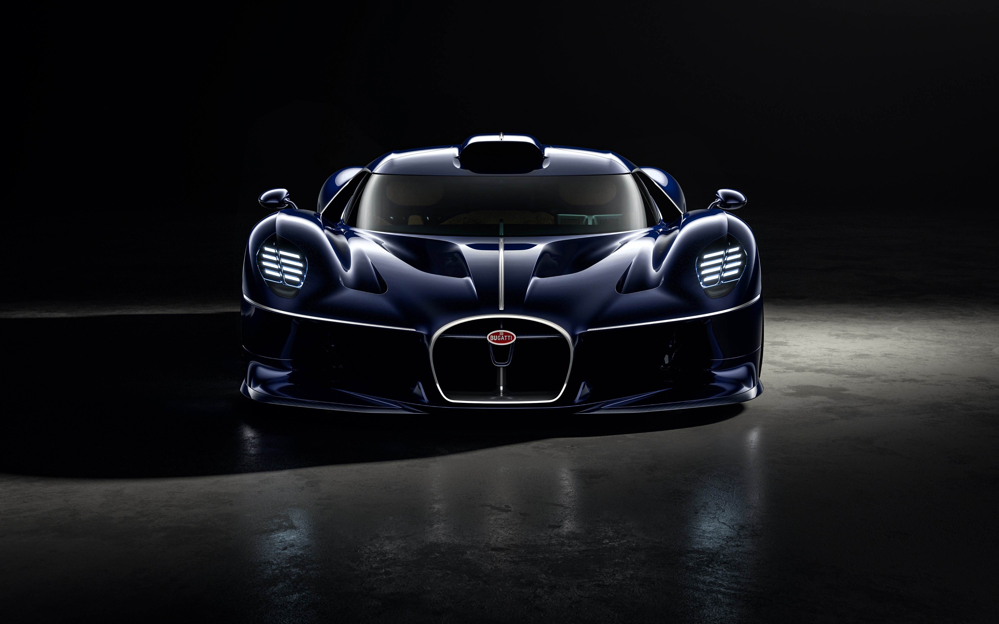 Carro esportivo Bugatti azul-marinho, visto de frente, com far&oacute;is acesos e grade frontal oval, em um ambiente escuro com reflexos no ch&atilde;o