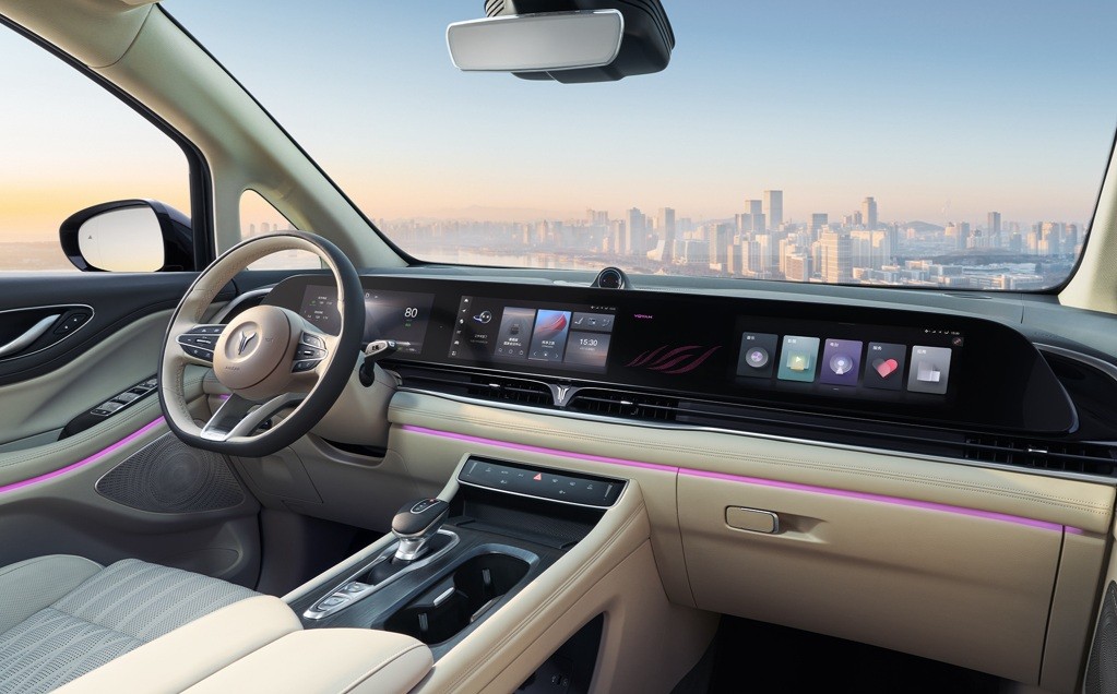 Interior de um carro moderno com painel digital e volante bege, detalhes em rosa neon e bancos claros. Ao fundo, uma cidade com arranha-c&eacute;us sob c&eacute;u azul