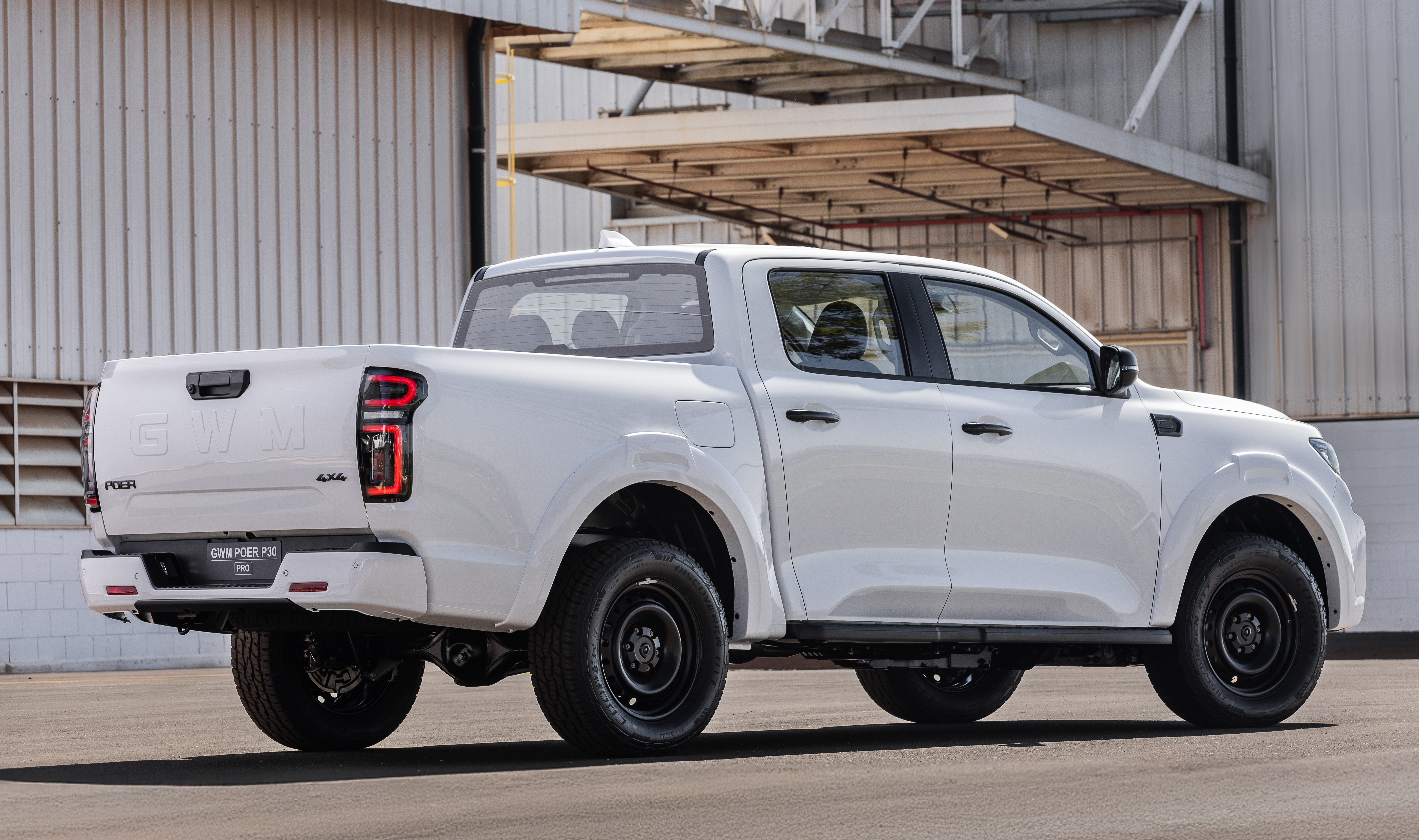 Picape branca GWM Poer King Kong 4x4, vista de traseira e lateral, estacionada em p&aacute;tio de concreto com um galp&atilde;o cinza ao fundo