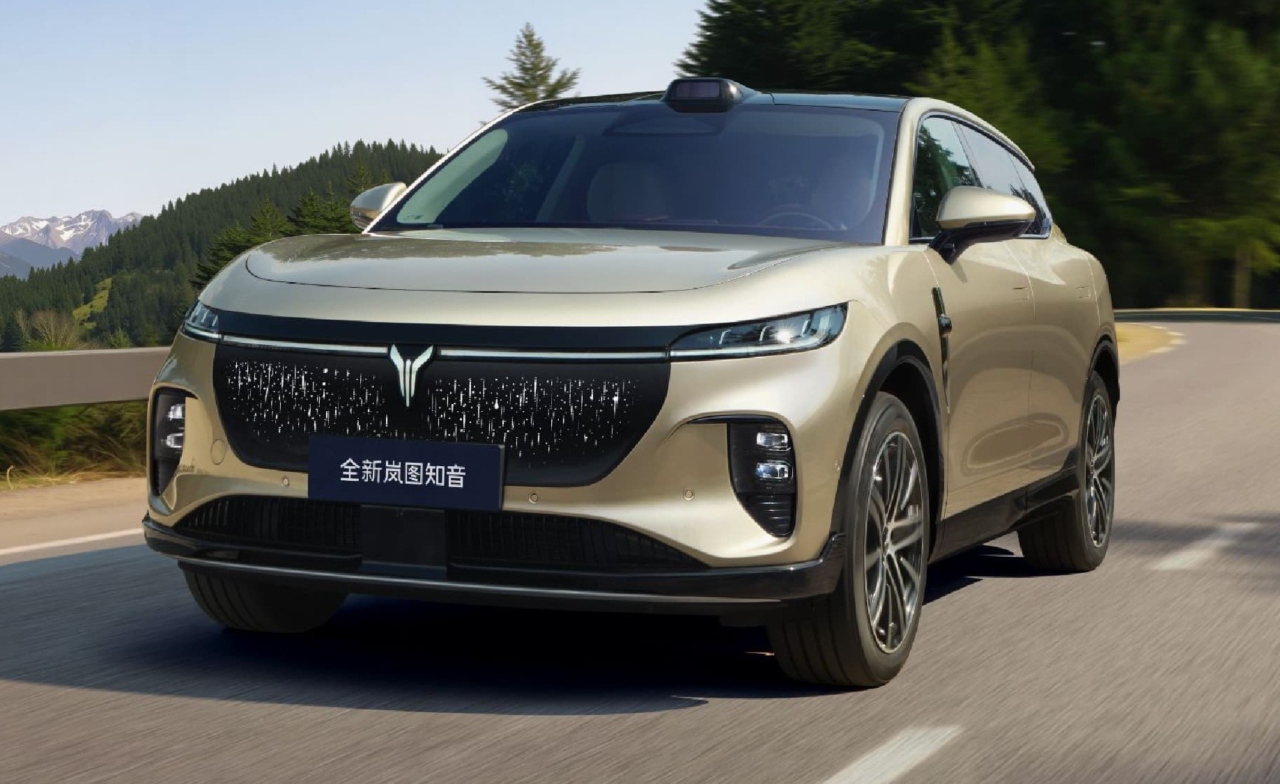 SUV dourado em movimento numa estrada sinuosa, com montanhas e &aacute;rvores verdes ao fundo. O carro tem uma grade frontal preta com um emblema prateado e um sensor preto no teto. Na placa frontal, l&ecirc;-se 全新岚图知音