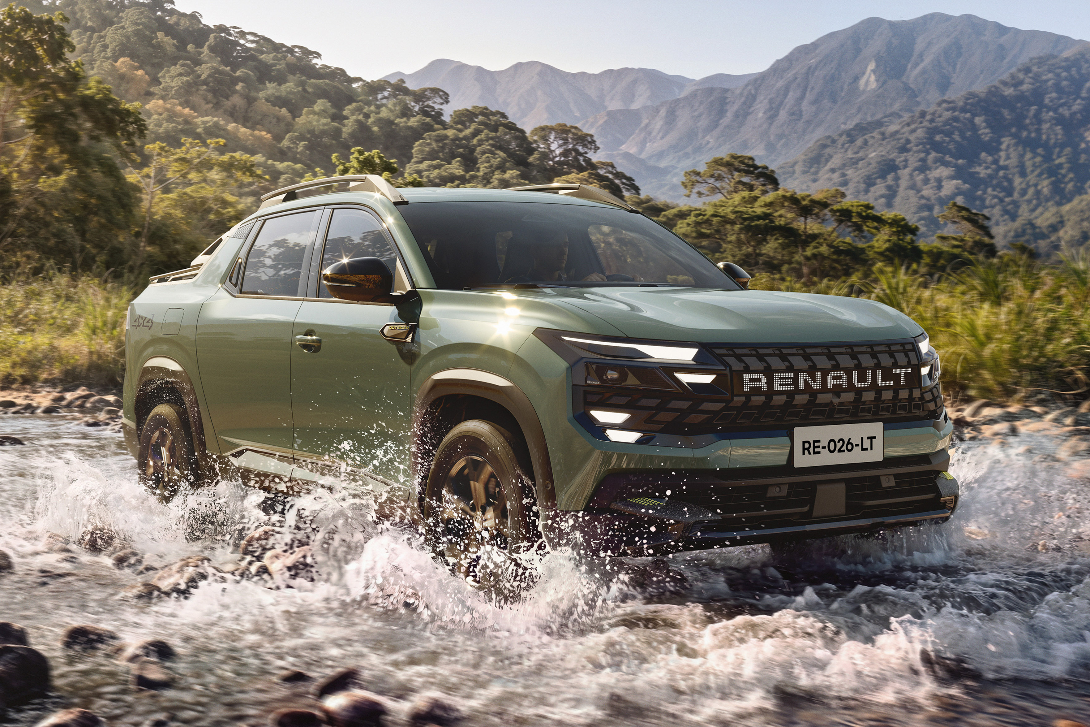 Picape Renault verde-oliva atravessando um rio raso, com água espirrando ao redor dos pneus. Ao fundo, montanhas e vegetação densa sob um céu claro